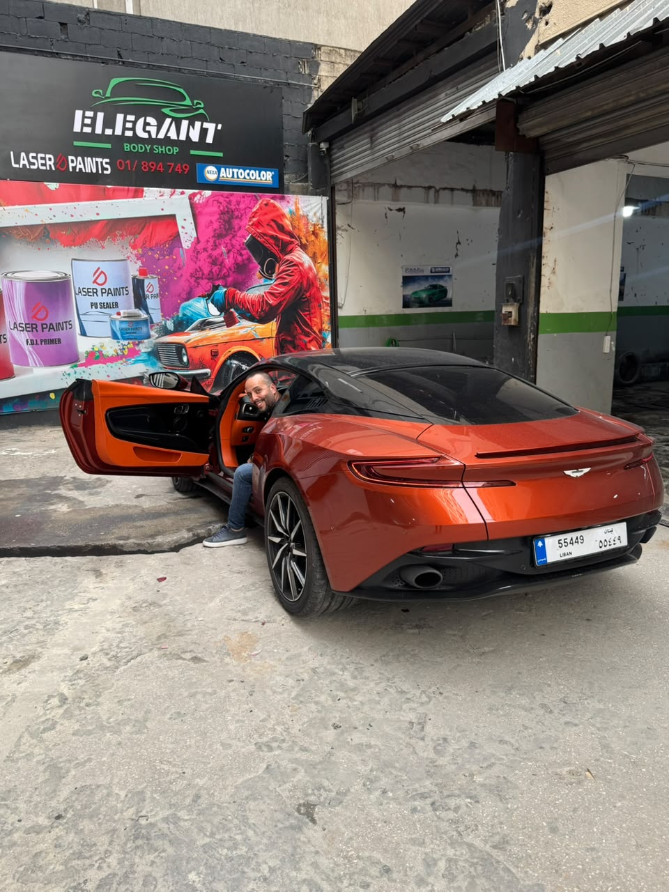 Raffi in an orange Aston Martin outside the garage