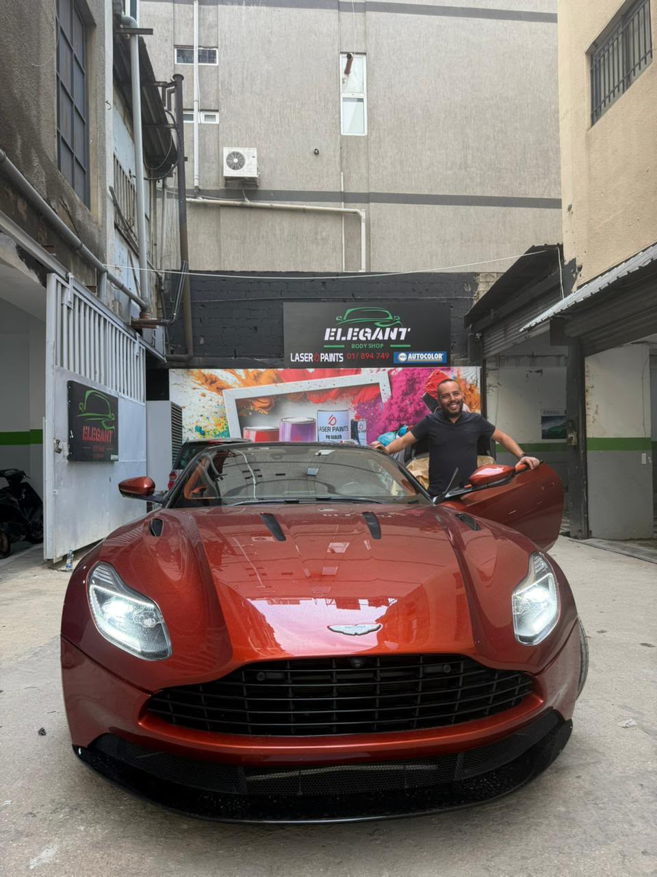 Raffi standing behind an orange Aston Martin at Elegant Body Shop